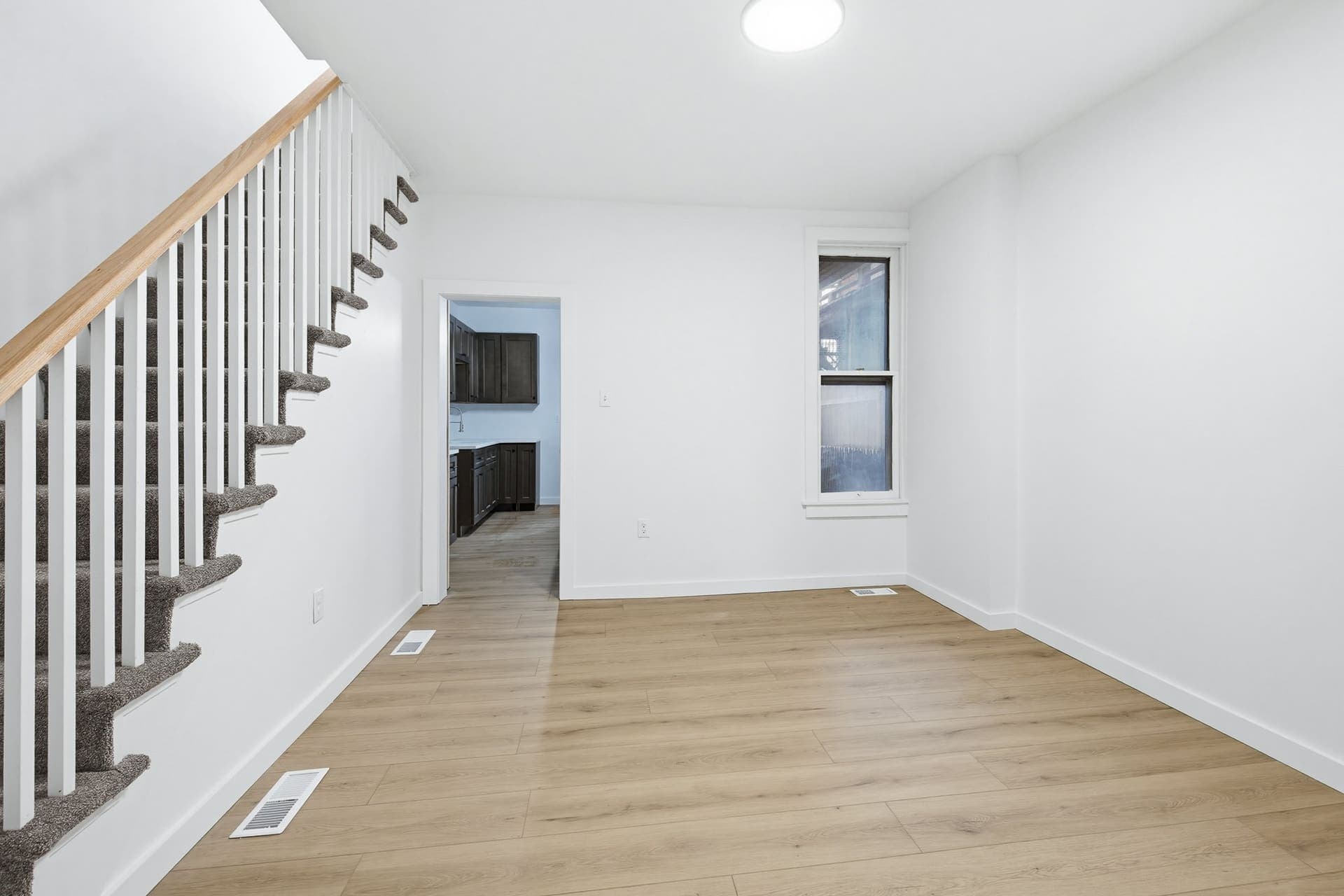 Stair hall with warm plank floors and kitchen beyond